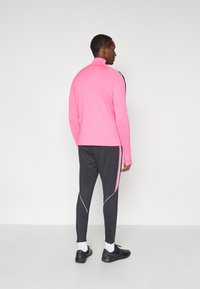 Εφαρμοστό ροζ μακρυμάνικο μπλουζάκι με ψηλό γιακά, συνδυασμένο με σκούρα γκρι αθλητικά παντελόνια που έχουν λευκές λωρίδες στο πλάι και φερμουάρ στους αστραγάλους. Μαύρα αθλητικά παπούτσια.