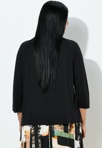 Czarna bluzka z rękawami do połowy przedramienia wykonana z miękkiej tkaniny, zestawiona z wielokolorową spódnicą w geometryczne wzory i motyw leśny.