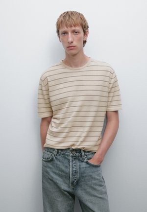 Cream striped t-shirt with short sleeves, round neckline, relaxed fit, paired with blue denim jeans. Textured fabric visible.