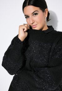 Maglione nero con un design testurizzato caratterizzato da fili lucidi, polsini a coste e un collo con sottili righe verticali. Tessuto lavorato a maglia morbido e spesso.
