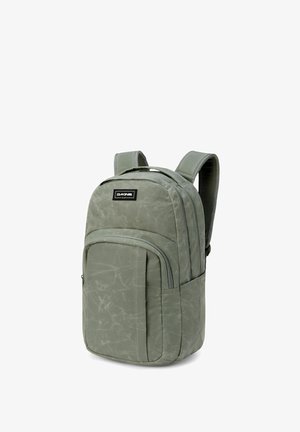 Sac à dos vert Dakine avec des bretelles rembourrées, une poche zippée à l'avant et un compartiment principal zippé, se tenant droit sur un fond blanc.