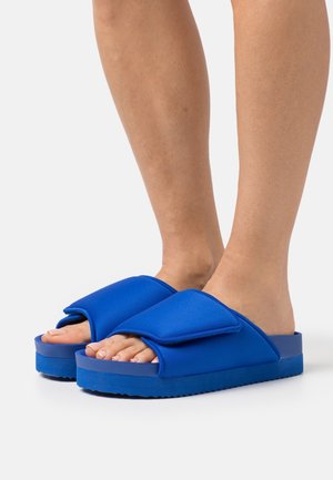Blå slide-sandaler med en tyk sål, tekstiloverdel og brede stropper. Den strukturerede fodseng giver godt greb. Pyntet med Velcro-lukninger.