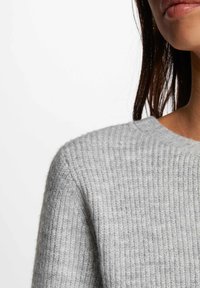 Grauer gestrickter Pullover mit Rippstruktur, der einen Rundhalsausschnitt und eine einfarbige Ausführung aufweist. Nahaufnahme der Schulter- und Ausschnittdetails.