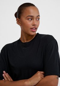 Sort kortærmet t-shirt med rund hals og et subtilt logo på kraven. Glat stofstruktur, afslappet pasform, med krydsede arme i en neutral pose.