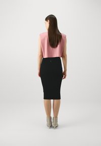 Rózsaszín, rövidujjús cropped top, amely fekete bordázott ceruzaszoknyával van párosítva, hajlékony sziluettjével és térd alá érő kialakításával.