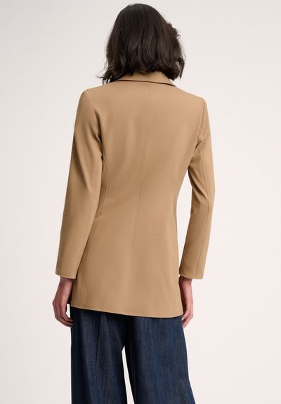Tan long-sleeve blazer with a tailored fit, featuring a notched collar, center seam detailing, and a smooth fabric texture.
