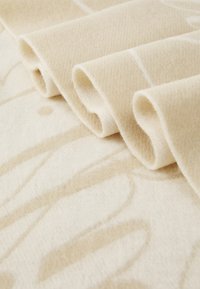 Beige fleece deken met zachte, opgerolde randen en een subtiel abstract patroon in lichtere tinten op een textuurstof.