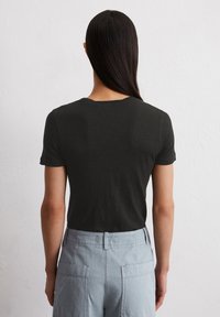 T-shirt noir à manches courtes avec un col rond, texture lisse et coupe ajustée, associé à un pantalon cargo bleu clair doté de poches latérales.