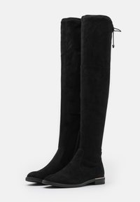 Botas negras de ante sobre la rodilla, con una textura suave y un zip lateral, con suela plana y un diseño minimalista.