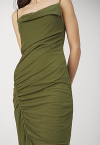 Olivgrön, figursydd klänning med en cowl-krage och rynkad textur, med tunna remmar och ett mjukt, elastiskt tyg.