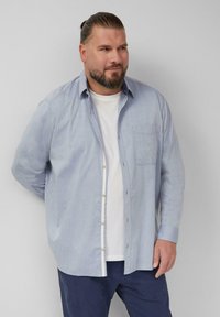 Lichtblauwe overhemd met lange mouwen en één borstzak, gedragen over een wit T-shirt, gecombineerd met een marineblauwe broek.