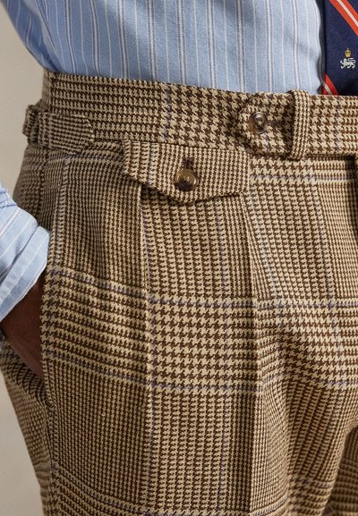 Maßgeschneiderte braune und beige Hahnentritt-Karo-Hose mit pattentaschen und Knöpfen, kombiniert mit blau gestreiftem Hemd und roter gemusterter Krawatte.