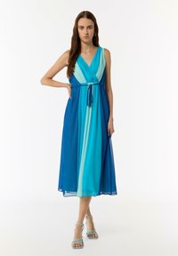 Ein ärmelloses, gerafftes Kleid in Farbverläufen von Blau, mit einem V-Ausschnitt, tailliertem Bund mit Kordelzug und fließendem Rock.