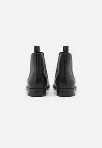 Botas Chelsea de cuero negro con textura suave, paneles laterales elásticos y lengüetas de tirón, con punta redonda y tacón bajo.