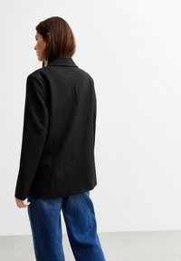 Blazer nero realizzato in tessuto liscio con una vestibilità su misura. Presenta un colletto classico, un taglio dritto e un retro aperto con dettagli minimi.