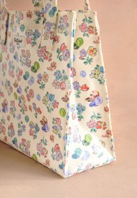 Borsa tote in tela con motivo floreale in colori pastello, caratterizzata da una forma rettangolare, due manici e un'etichetta sul lato.