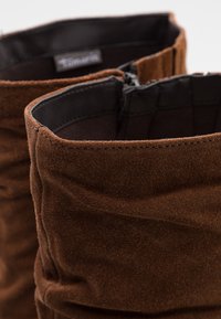 Bottes cheville en daim marron au design décontracté, avec une doublure intérieure lisse et une fermeture éclair sur le dessus. Extérieur texturé.