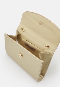Zlatá kabelka typu clutch s elegantním designem, vybavená zapínáním na knoflík a vnitřními přihrádkami. Hladký povrch s viditelným logem značky.