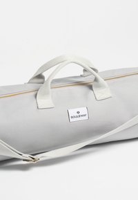 Bolsa de lona gris con asas blancas, un cierre dorado y una etiqueta. Presenta una forma cilíndrica y una correa de hombro desmontable.