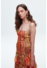 Tr�ägerloses Kleid in gemischten Mustern aus Rot, Orange und Gold, mit einem Rüschensaum und einer gerafften Textur im gesamten Oberteil.