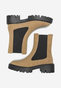 Botas Chelsea de cuero marrón claro con paneles elásticos en los costados, suelas de goma y acentos texturizados en negro. Las suelas gruesas y dentadas proporcionan agarre.