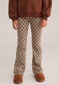 Brun sweatshirt i kombination med mönstrade utsvängda byxor med ett geometriskt mönster i brunt och beige, kompletterat med bruna skor.