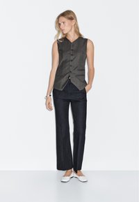 Sleeveless gray vest with button closure, paired with dark blue wide-leg trousers and white shoes. Simple design, tailored fit, minimal detailing.