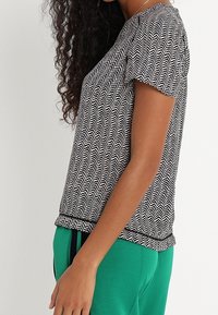 Top corto de manga corta con un patrón de zigzag en blanco y negro, con cuello redondo y ajuste relajado, combinado con pantalones verdes.