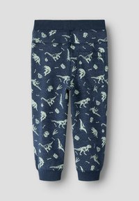 Tummansiniset verkkohousut, joissa on vaaleanvihreä kuvio dinosauruksista ja fossiileista. Pehmeä materiaali, jossa joustava vyötärö ja takatasku.