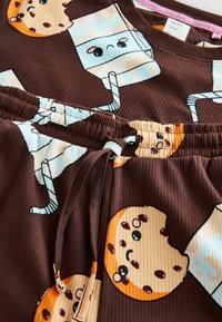 Brown ribbed fabric featuring a playful pattern of cookies and milk cartons with cartoonish faces. Elastic waistband with drawstring detail.
