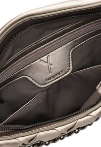 Wnętrze metalicznie szarej torebki z zamykanymi na zamek przegródkami oraz gładkim, teksturowanym wykończeniem. Posiada naszywkę z logo oraz subtelne detale w postaci przeszyć.