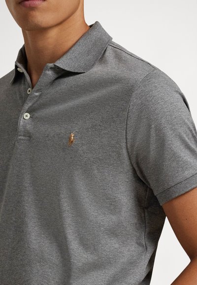 Pelēka polo krekls ar trīs pogu aizdari, īsām piedurknēm un nelielu izšūtu logotipu brūnganā krāsā kreisajā krūšu daļā. Mīkstas auduma tekstūra.