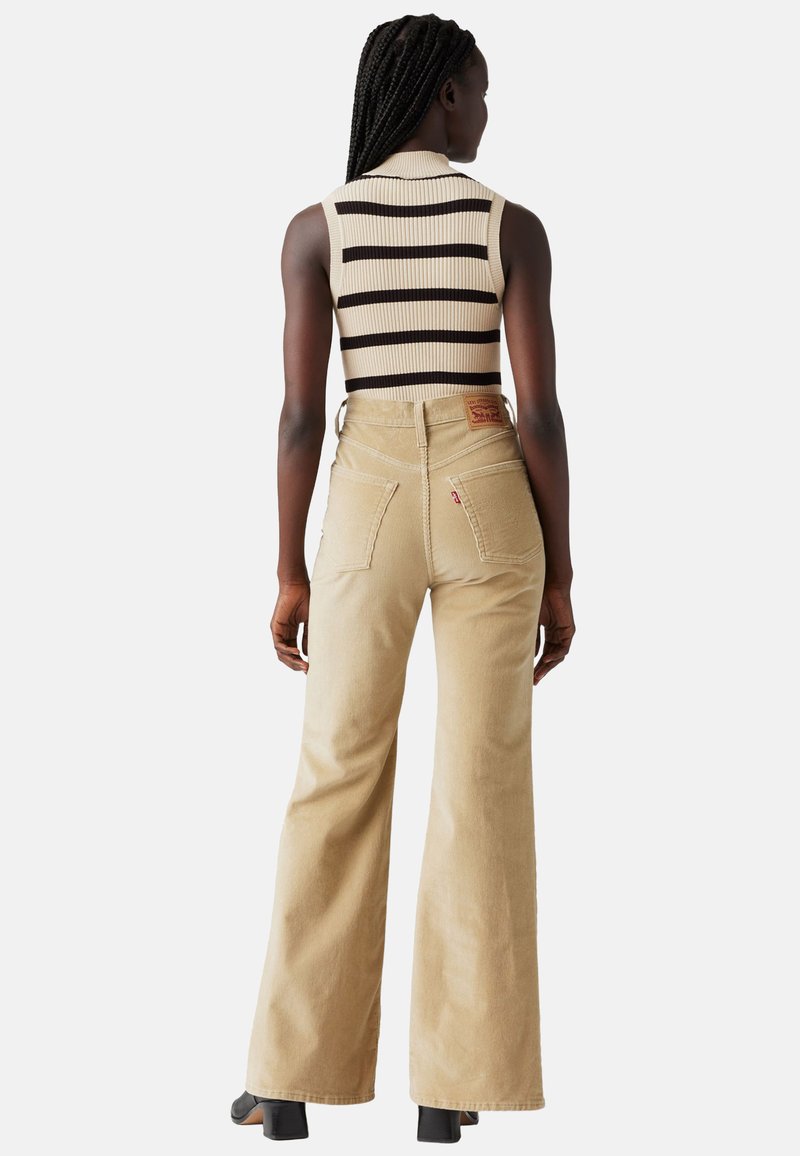 Jean large beige à taille haute avec deux poches arrière. Associé à un haut sans manches à rayures côtelé en crème et noir.