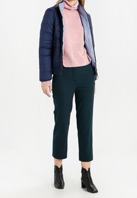 Námořnická péřová bunda se světle šedou podšívkou, růžový rolák, tmavě zelené zúžené kalhoty a černé kotníkové boty.