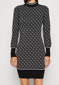 Robe noire à manches longues avec motifs losanges blancs, col et poignets côtelés, coupe ajustée, longueur genou, tissu en maille texturé.