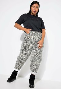 Camiseta gráfica negra con texto "INTENSE", combinada con pantalones joggers de estampado de leopardo beige y botas negras de tobillo. Puños enrollados en los pantalones.