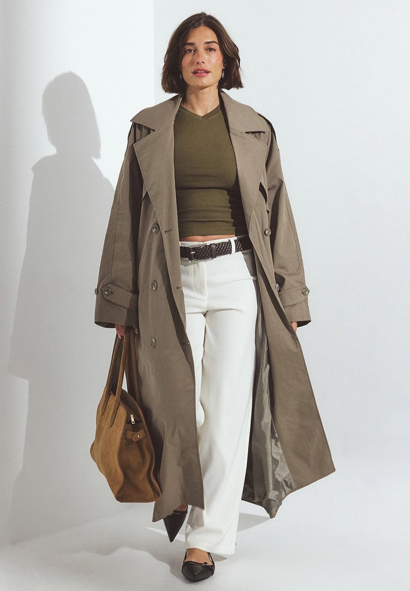 Gai brūns tranšejas mētelis ar lielām pogām, virs olīvzaļa pieguļošā topa. Balti brīvi iegarenie bikses, melni dzīvokļi un brūna zamšāda somiņa.