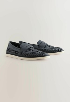 Tmavě šedé slip-on boty s pletenými detaily, hladkým svrškem, gumovou podrážkou a kontrastním bílým okrajem. Měkká textura a uvolněný design.