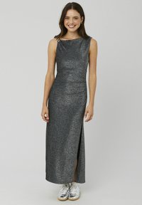 Robe argentée scintillante longue jusqu'au sol avec une fente latérale, dotée d'un col froncé et d'un détail orné à l'épaule, portée avec des baskets blanches.