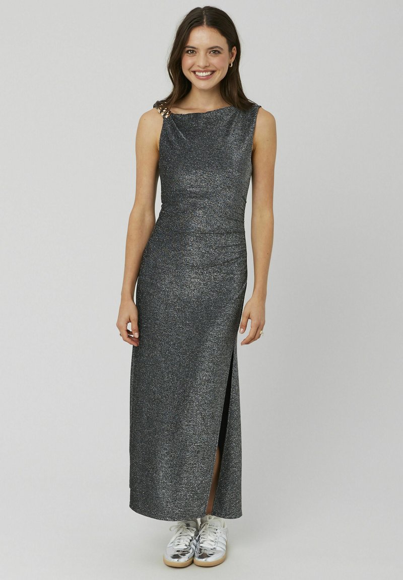 Robe argentée scintillante longue jusqu'au sol avec une fente latérale, dotée d'un col froncé et d'un détail orné à l'épaule, portée avec des baskets blanches.