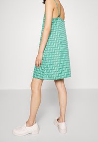 Zelené šaty bez rukávů s volným střihem, zdobené geometrickým vzorem. V kombinaci s světle růžovými nazouvacími botami.