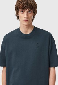 Czarny, ciemnoszary T-shirt bawełniany z krótkimi rękawami, okrągłym dekoltem i małym czarnym logo na piersi. Gładka tekstura, luźny krój.