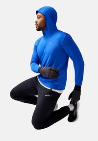 Blaues langärmliges Sportshirt mit Kapuze und Reißverschlusskragen, kombiniert mit schwarzen Laufhosen. Schwarze gefütterte Handschuhe und Laufschuhe sind ebenfalls enthalten.