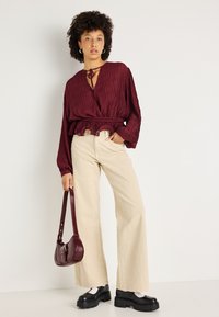 Blusa texturizada burgundy com decote amarrado, combinada com calças largas em creme. Sapatos de plataforma pretos e uma pequena bolsa burgundy completam o look.