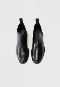 Par de botas de cuero negro pulido de tipo slip-on con tiradores, vistas desde arriba sobre fondo blanco liso.