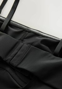 Zwarte sportkleding van een gladde, textuurstof met dunne bandjes en een contrasterende grijze rand langs de bovenkant. Strak ontwerp met minimale naden.
