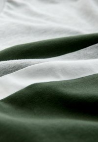 Close-up van stof met afwisselend dikke horizontale strepen in donkergroen, lichtgrijs en wit, met zichtbare textuur en plooien.