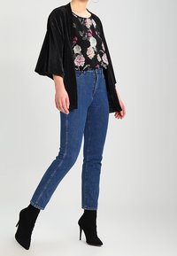 Kimono de pana negro, blusa floral con patrones multicolores, jeans de tiro alto azules y botines negros.