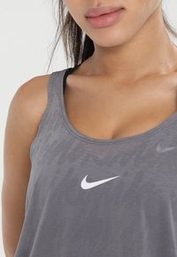 Gros plan d'une personne portant un débardeur Nike gris avec un logo swoosh blanc au centre de la poitrine.