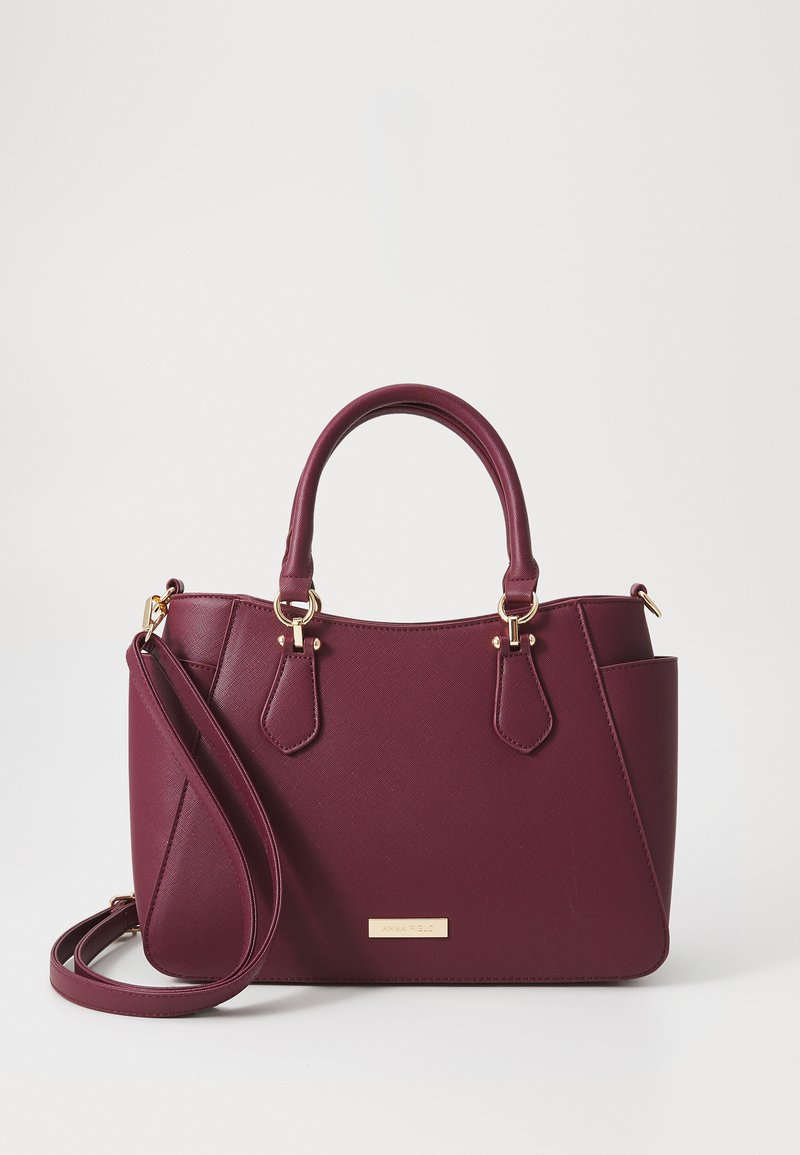 Borsa sintetica color bordeaux con doppio manico superiore, dettagli in hardware dorato e una tracolla rimovibile. Superficie texture con tasche laterali.
